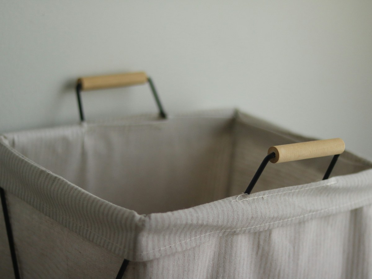 An empty, light-colored laundry hamper with wooden handles