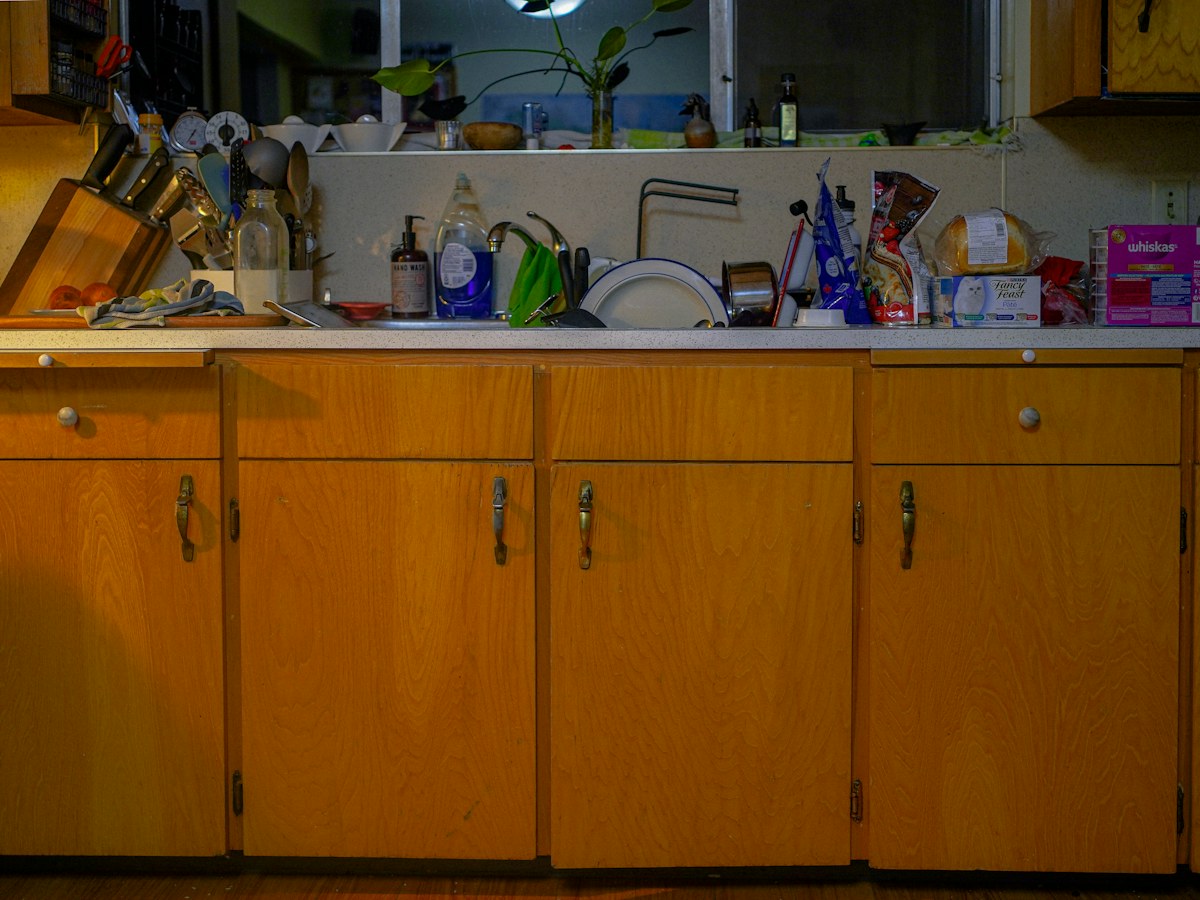A cluttered kitchen counter with wooden cabinets below
